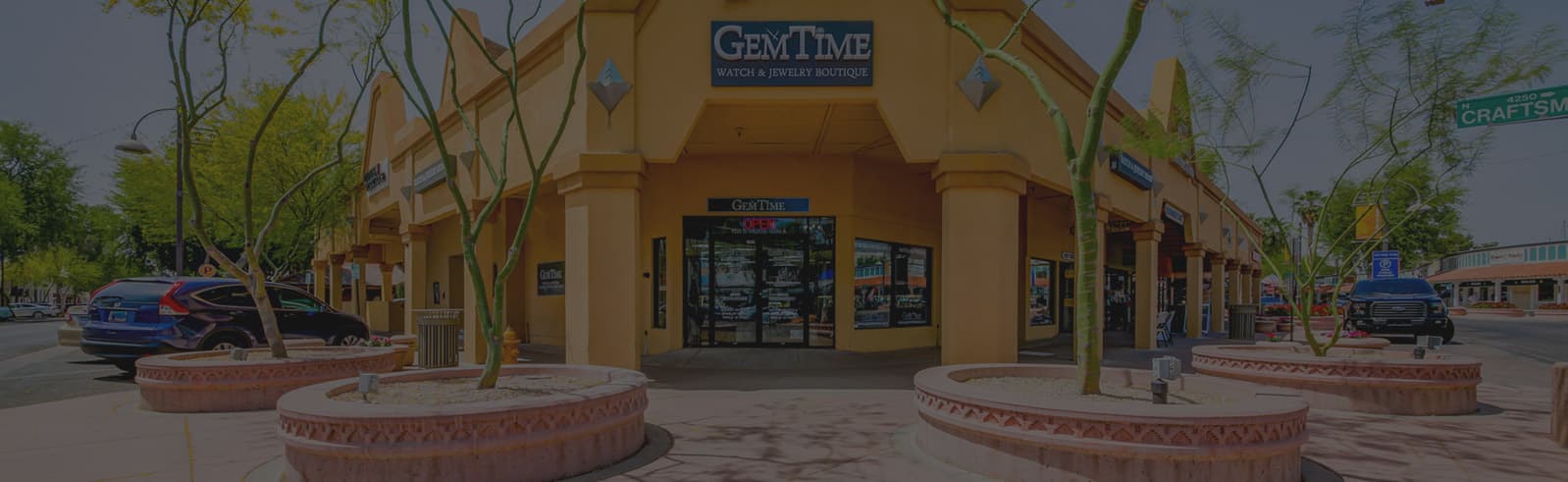 Tan stucco storefront with GemTime signage, columns, and desert landscaping