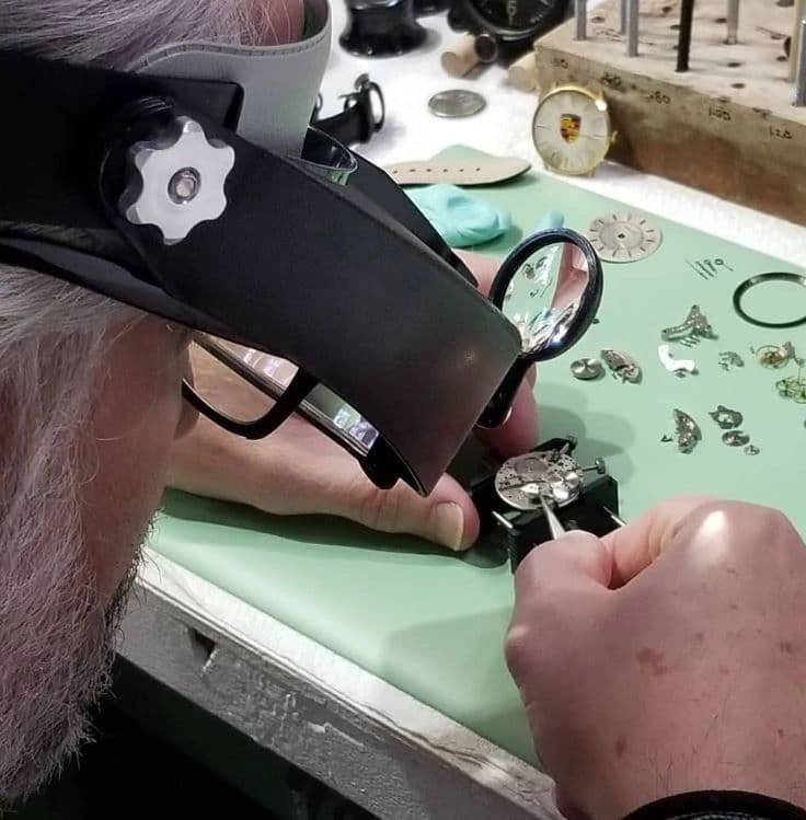 Person examining watch components and repair tools on work surface